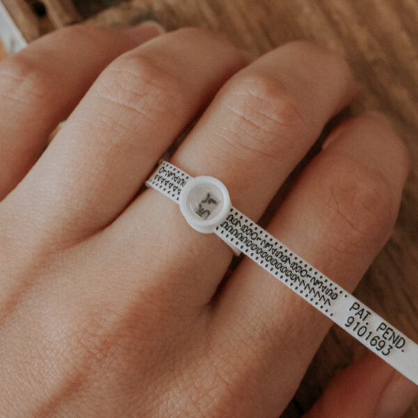 een hand waarop aan één vinger de ringsizer wordt gebruikt om te demonstreren hoe je je ringmaat op kan meten